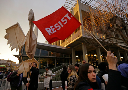 Photo of someone holding a giant dove made of cloth and sticks. Another person holds a red flag that says RESIST.
