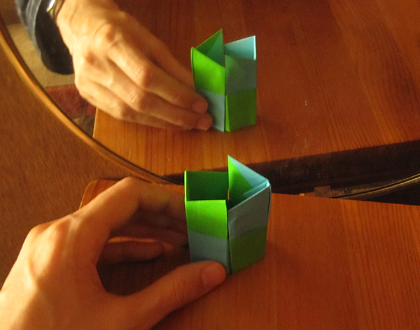 An origami arrow in front of a mirror. The arrow points to the left, while the reflection points to the right.