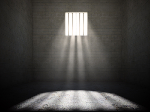 A prison cell with light streaming through a barred window