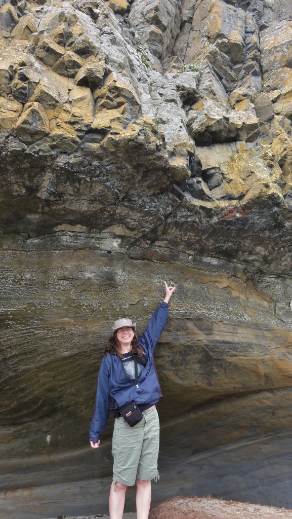 Image shows me standing under a lip of massive basalt, in front of streaky sandstone rocks that the basalt overlies.