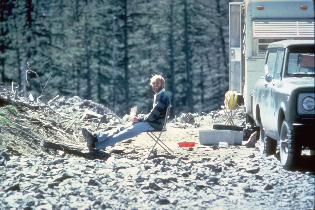 Image shows a bearded Dave Johnston sitting in a camp chair with his feet up, smiling at the camera. A forest stands behind him.