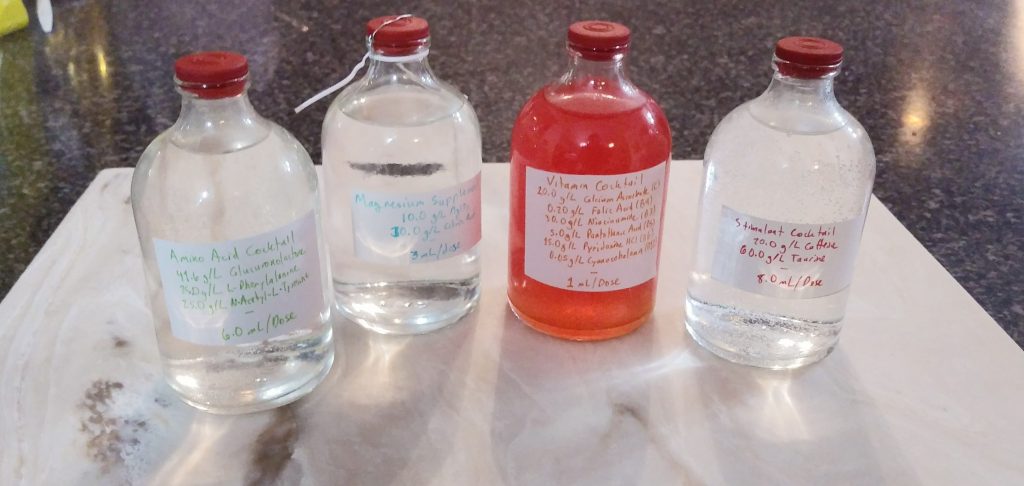 Four small labelled bottles, three containing clear liquid and one, the third, containing reddish-orange liquid.