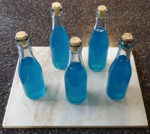 A collection of five small stoppered glass bottles, all containing a cyan-blue liquid.