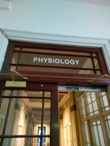 A photo of a set of double doors. The focus is on the label 'Physiology' written on the glass above the doors.