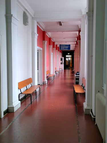 A photo of a hallway painted pink and white. Distinctive benches made of oblong planks are visible running the length of the hallway.