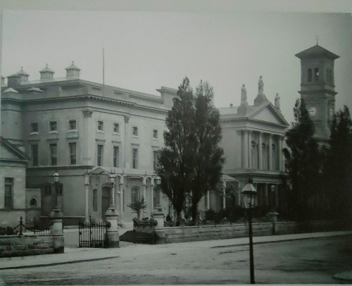 A photo of the previous building, clearly an older version. There is a front section with a cornice and pillars that is missing from the modern image.